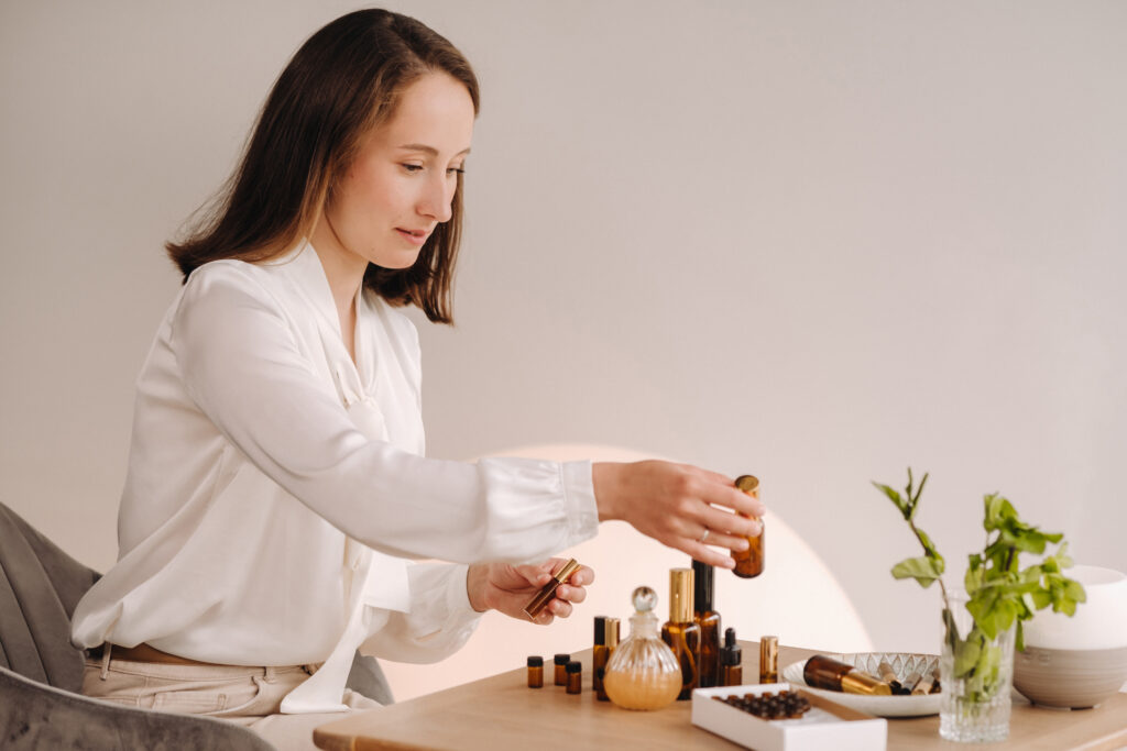 Mulher manuseando varios frascos de óleos essenciais em uma mesa de madeira clara